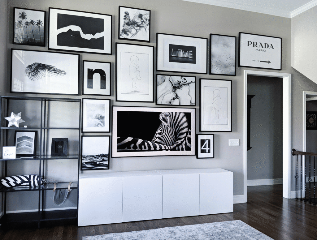 Modern living room with a large black and white gallery wall featuring zebra art, abstract prints, typography pieces, and minimalist line drawings above a low white media cabinet and open black shelving.