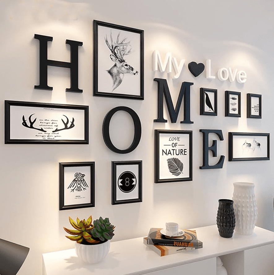 Modern gallery wall with black and white budget frames and bold letters spelling HOME, arranged above a white console with small plants, books, and vases.