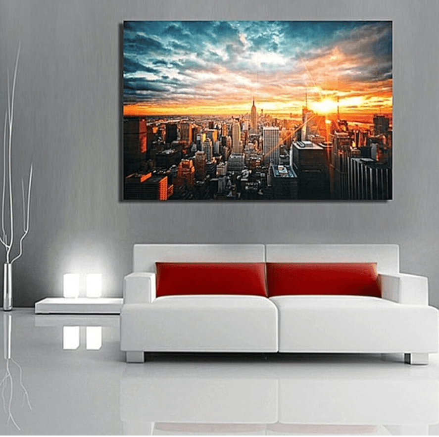 Minimal gray living room with a white sofa and red cushions, featuring a large framed city skyline photo with a dramatic sunset mounted above the couch.