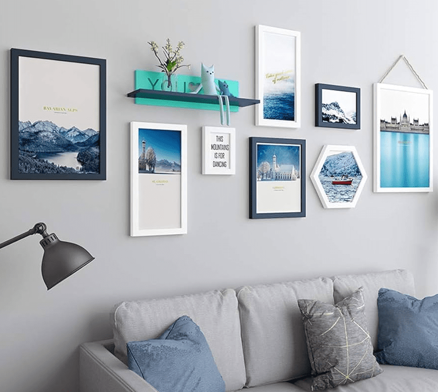 Mixed white and black picture frames in varied sizes on a light gray wall above a pale sofa, featuring blue toned prints and a small teal shelf with decor.