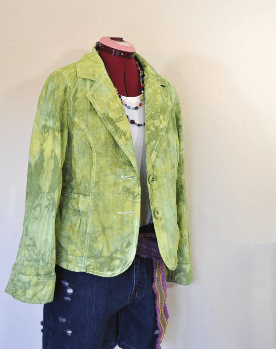 Upcycled lime green tie dyed blazer styled over a white top with dark distressed denim shorts on a dress form, creating a bold sustainable outfit.