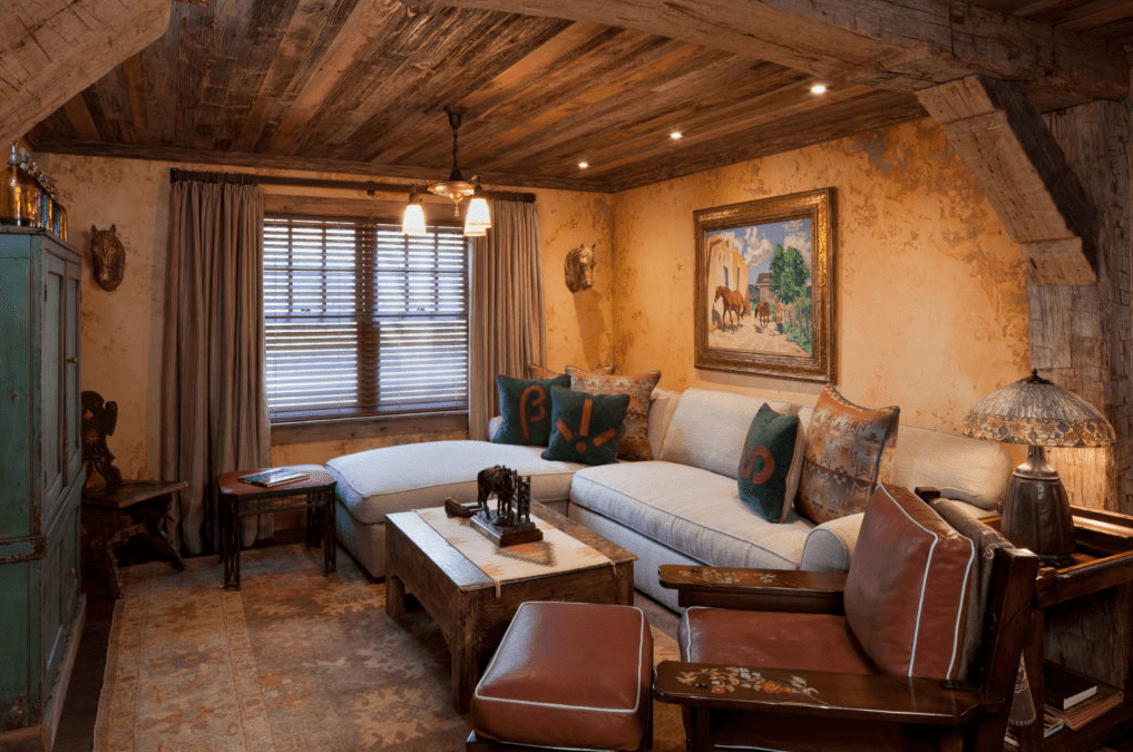 Rustic living room with reclaimed barn wood ceiling and beams, a light sectional sofa, leather armchairs, and warm ambient lighting.