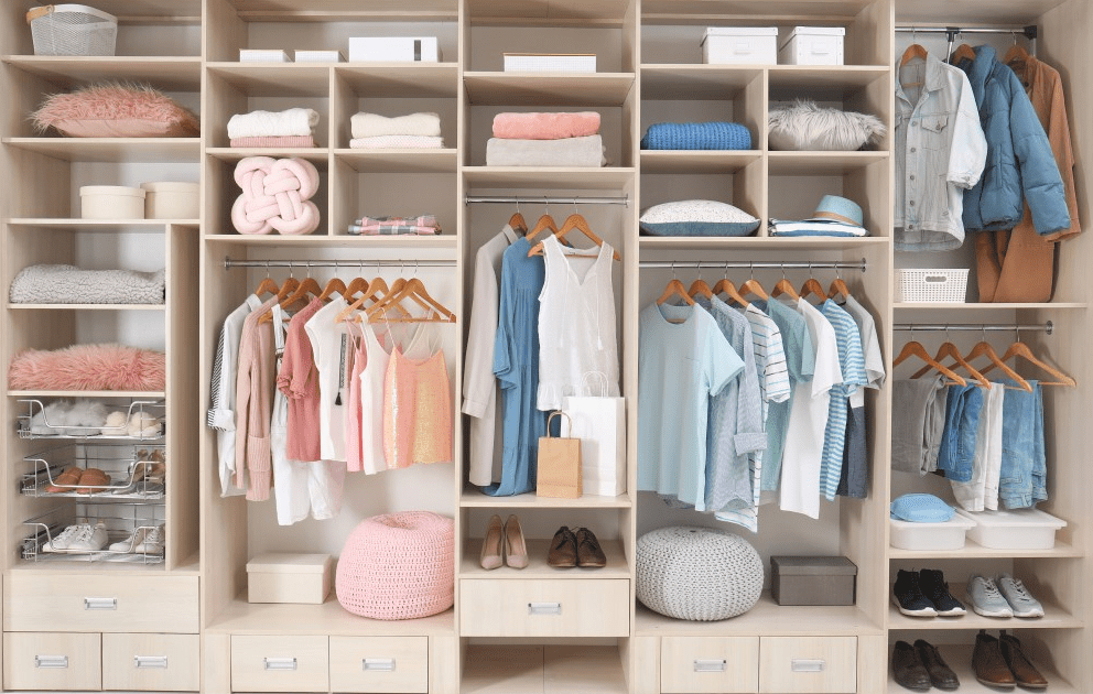 Organized open closet with folded sweaters, baskets, and color coordinated clothes showing tidy long term seasonal storage.