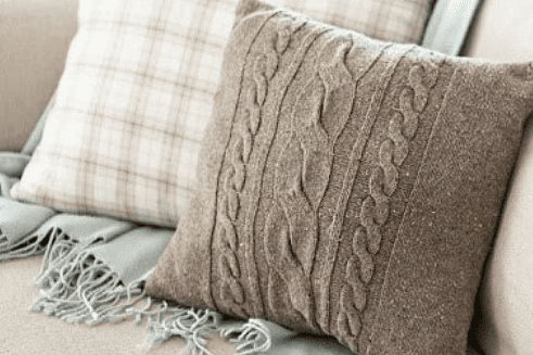 Cozy cable knit pillow made from an old sweater on a sofa with a plaid cushion and soft throw blanket