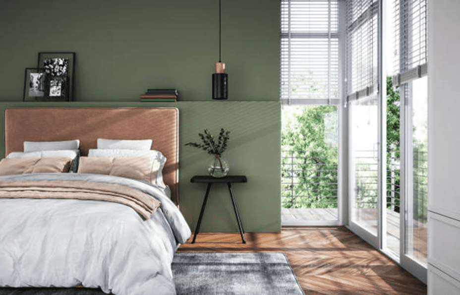 Modern bedroom with a soft green feature wall, upholstered headboard, white and beige bedding, wood floor, and tall windows letting in natural light from a balcony