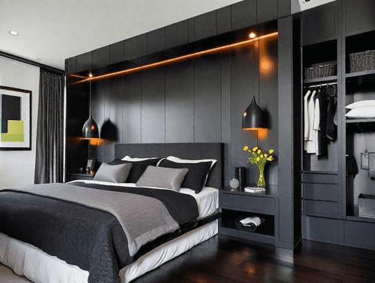 Modern bedroom with floor to ceiling dark wardrobes behind the bed, warm strip lighting, black pendant lamps, gray layered bedding, and an open closet section with neatly arranged clothes